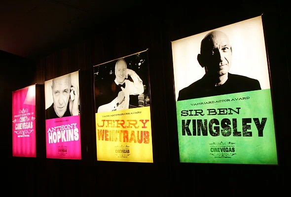 Illuminated CineVegas award banners featuring Anthony Hopkins, Jerry Weintraub, and Sir Ben Kingsley hang along a dark wall.