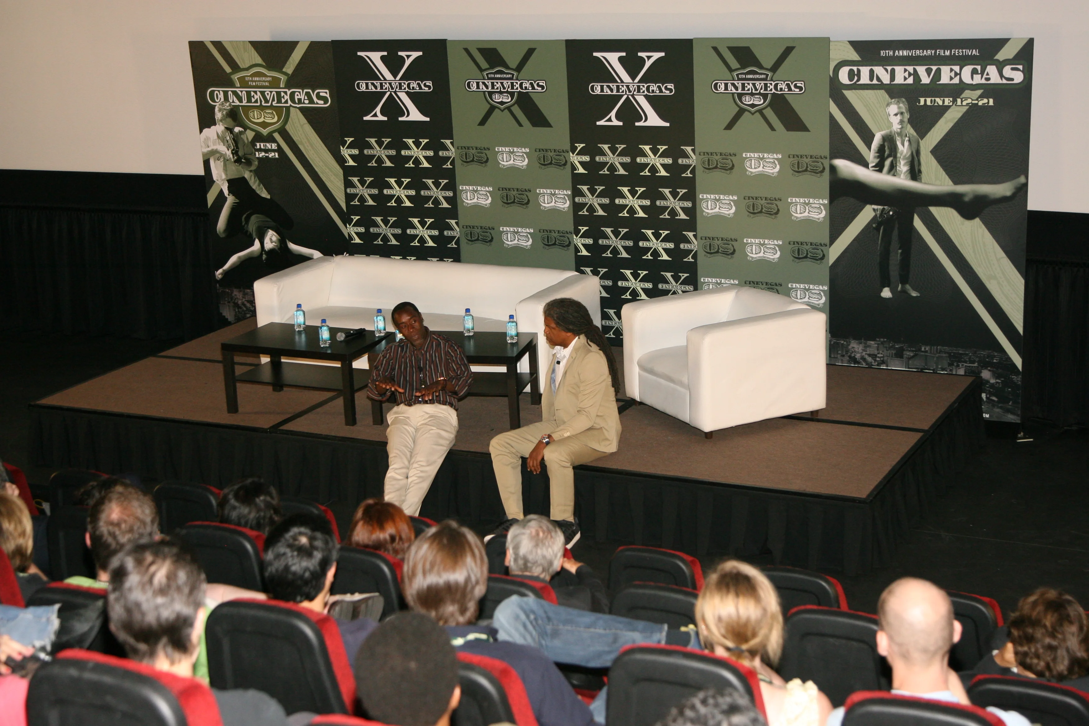Q&A staging — the branded backdrop for post-screening Q&A sessions, with a panelist on stage and an audience visible from behind. The poster's imagery repeats across the full width.